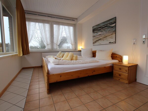 A bedroom with a wooden bed, white bedding, a nightstand, a lamp, and a painting on the wall.