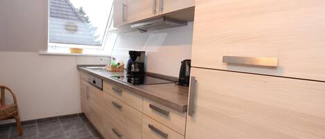 A modern kitchen with light wood cabinets, a black countertop, and a window above the sink.
