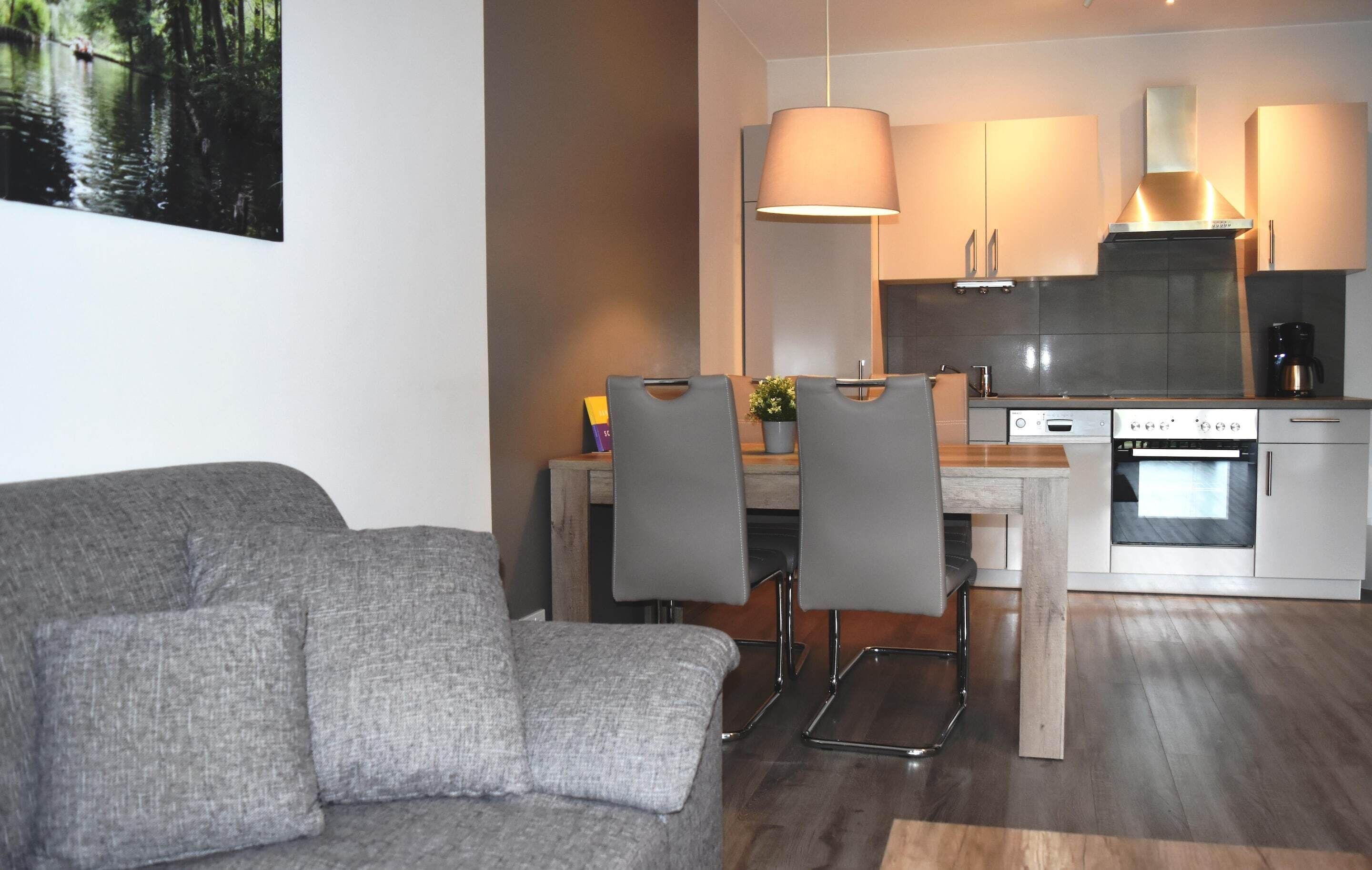Una cocina moderna con zona de comedor, sofá gris y vistas a un bosque.