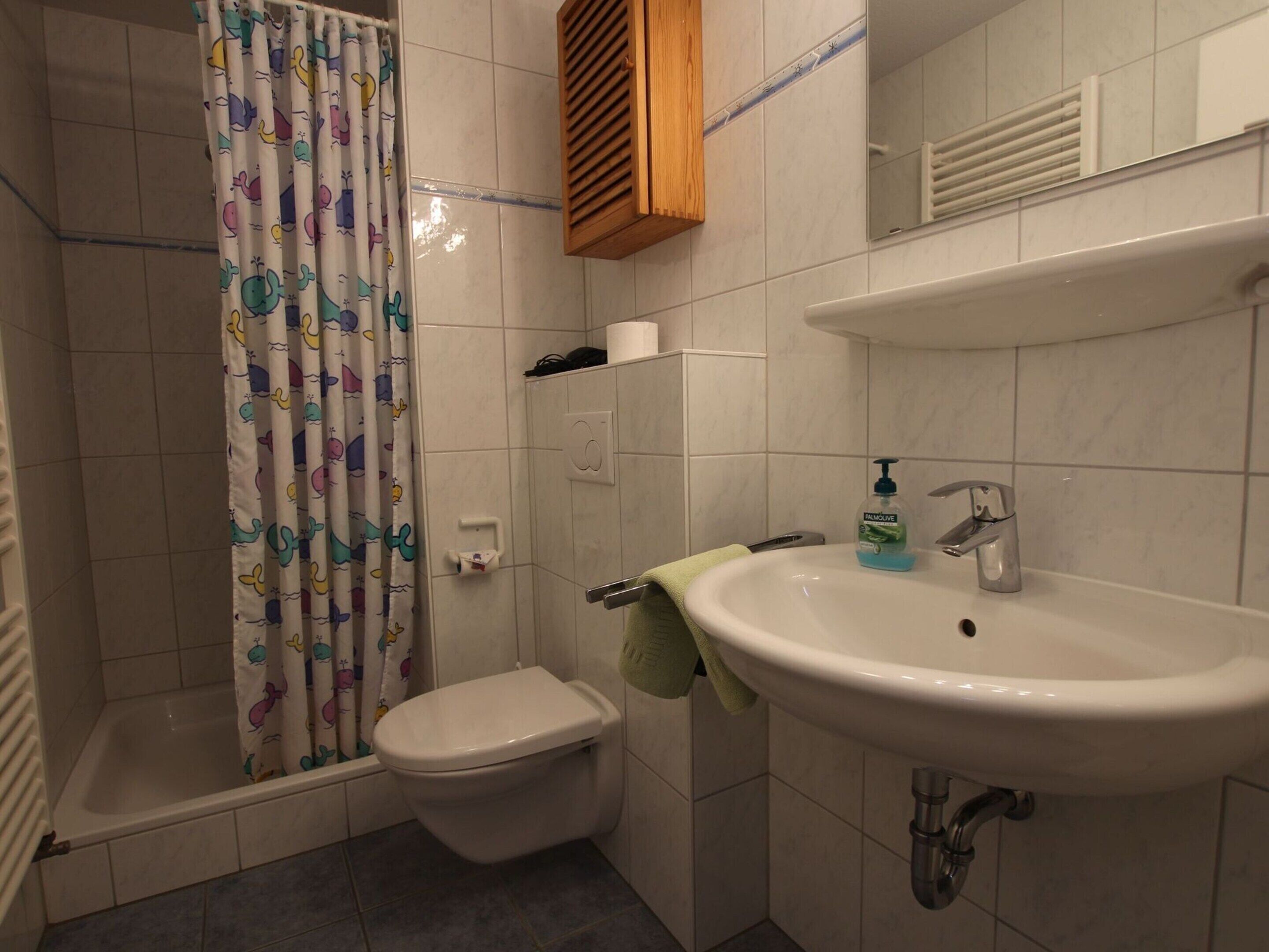 A bathroom with a toilet, shower, sink, and a towel rack.