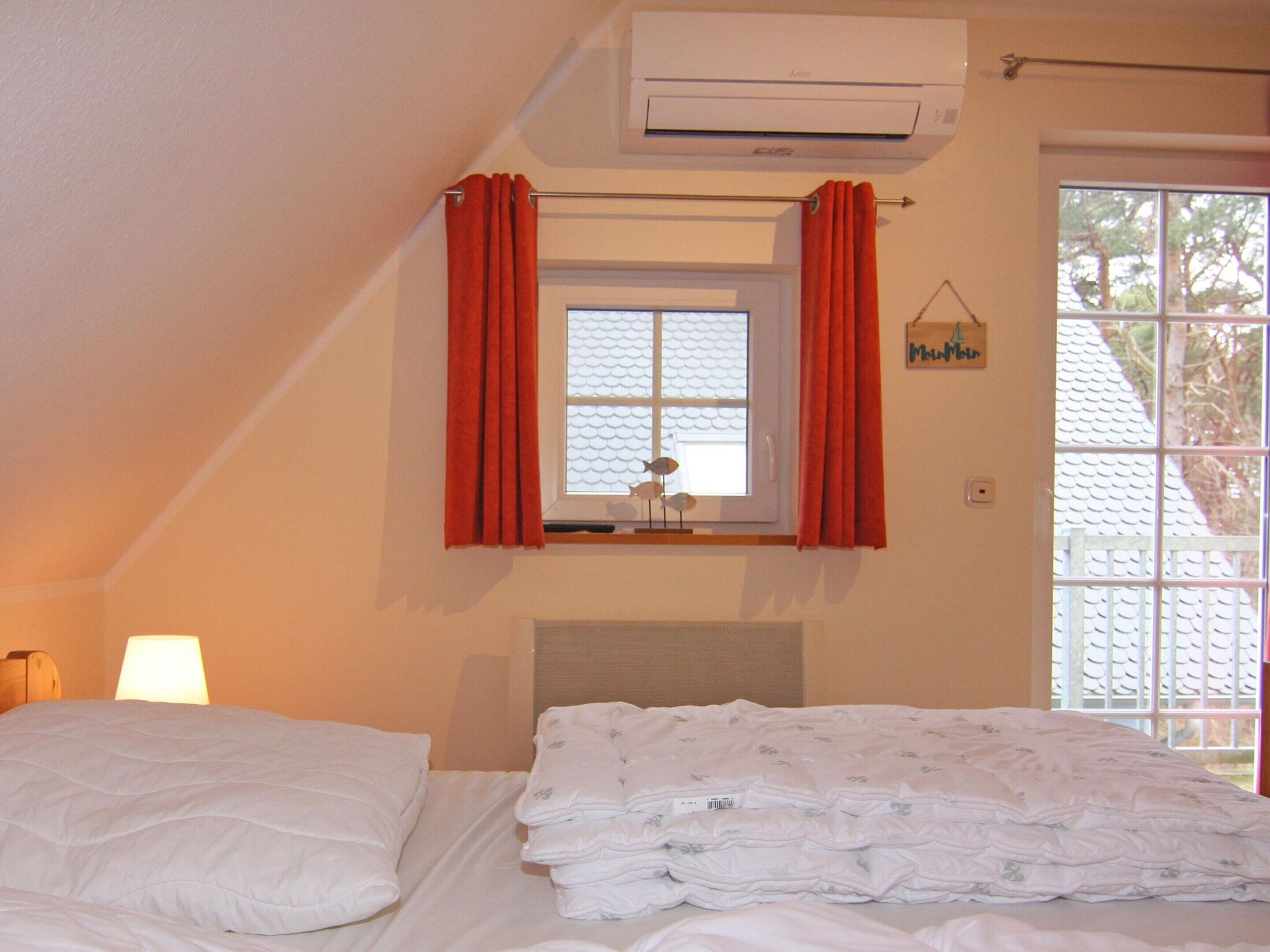 A bedroom with a bed, a window with curtains, an air conditioner, and a view of trees outside.