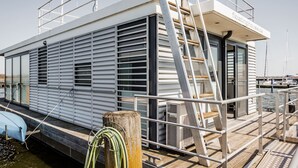 Una casa flotante con terraza, barandillas y escalera que lleva a la entrada.