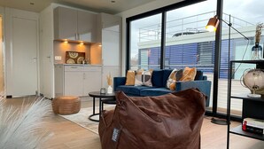 Una sala de estar moderna con un sofá azul, un sillón de peluche marrón y una mesa de centro de vidrio.