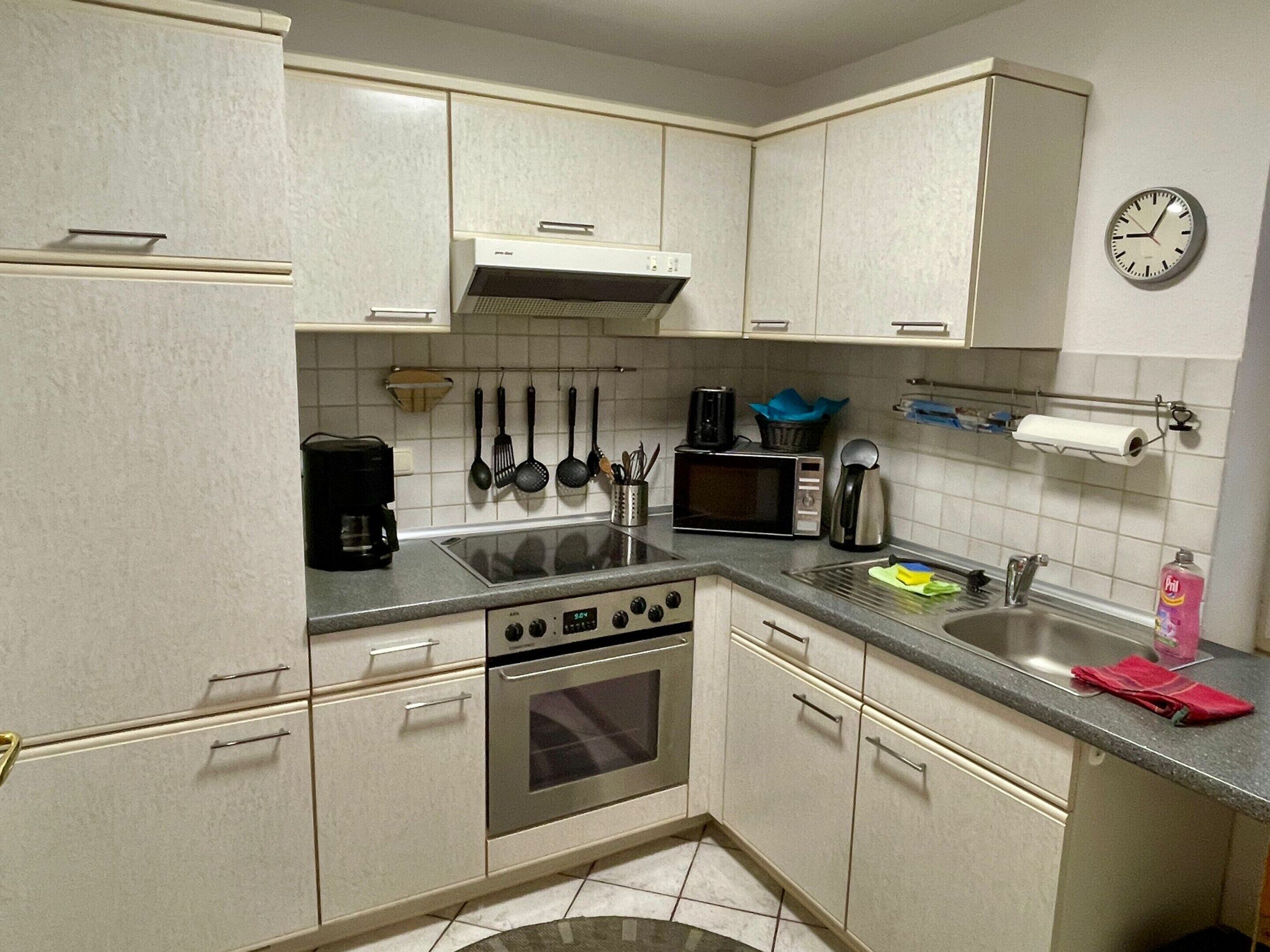 A kitchen with white cabinets, a microwave, stove, and a clock on the wall.