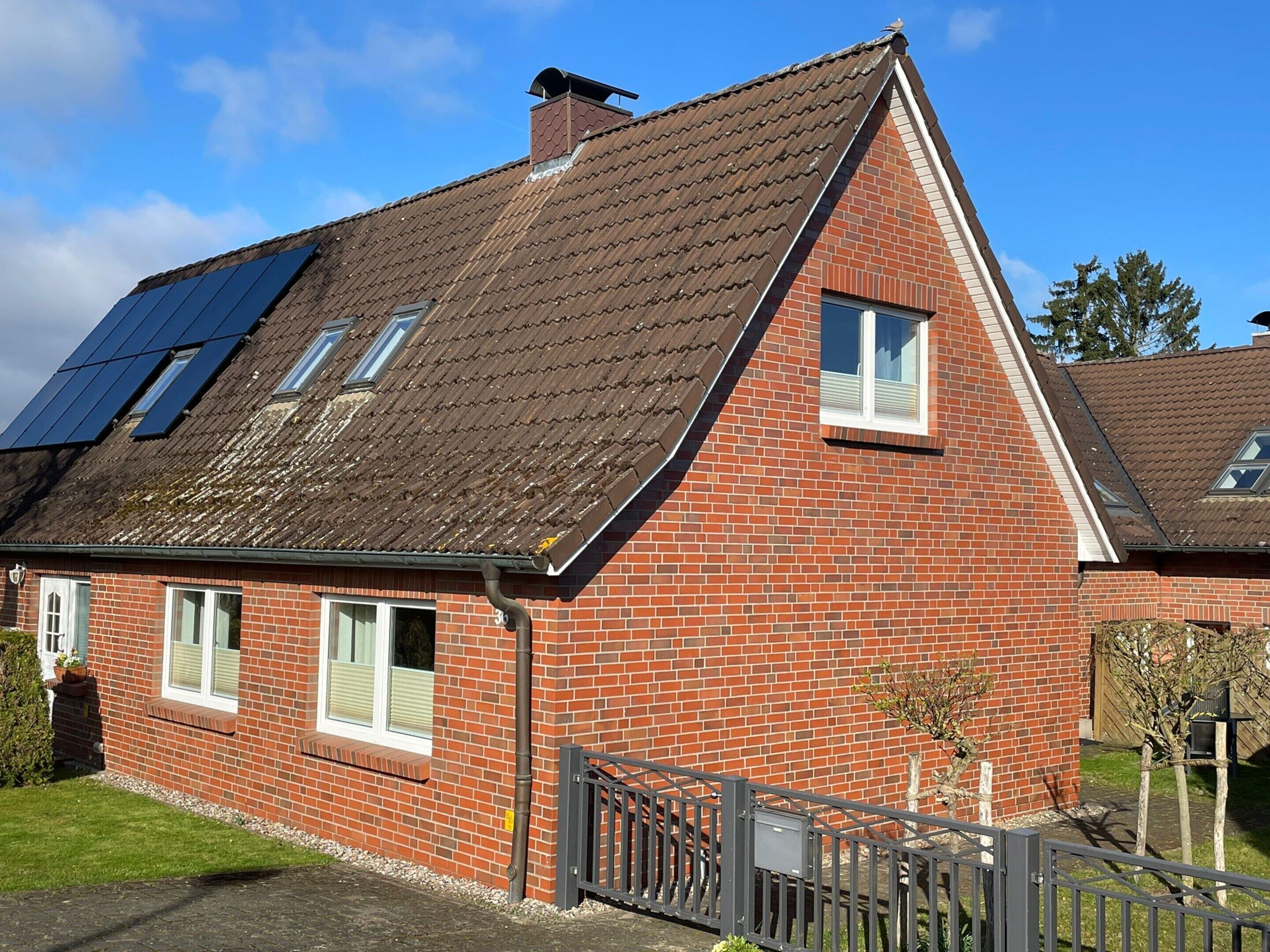 Et hus med skråt tag, solpaneler, facade i mursten og en lille forhave.
