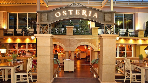 A hotel lobby with a prominent 'OSTERIA' sign, wooden furniture, and a view of the interior dining area. - Appartements im Freizeitpark Weissenhauser Strand (Wangels)