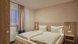 A double bed with two pillows, a bedside table, a wall-mounted lamp, and a window with curtains. - Appartements im Freizeitpark Weissenhauser Strand (Wangels)