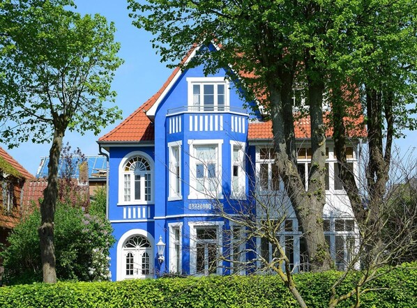 A blue building with a red roof, surrounded by trees and other buildings. - Appartement, Wyk auf Fohr (Wyk auf Foehr)