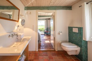 A bathroom with a bathtub, toilet, and a view of a garden through an open door.