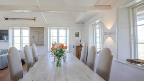 Une salle à manger avec une longue table en bois, six chaises rembourrées et un vase rempli de fleurs.