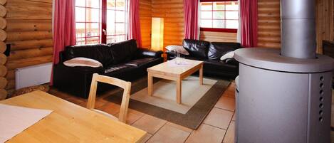 L’intérieur d’un chalet en rondins, avec deux canapés en cuir noir, une table en bois et un poêle à bois.