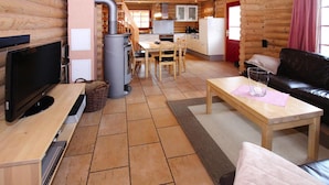 Interior de uma cabana de tronco com sala de jantar, cozinha, sala de estar e uma televisão sobre uma mesa de madeira.