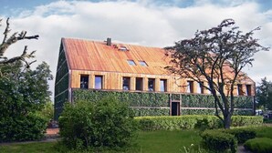 A modern house with a sloped roof, wooden exterior, and a garden with hedges and trees. - Ferienhaus Bel Ami, Nakenstorf (Zurow)