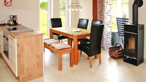 A modern kitchen with a built-in stove, a dining area with a wooden table and chairs, and a view of the outdoors through large windows. - Ferienhaus Bel Ami, Nakenstorf (Zurow)