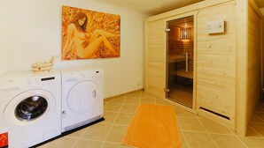 Un área de lavandería con dos lavadoras, una sauna de madera y una toalla en el suelo.