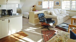 Una sala de estar acogedora con un sofá blanco, un sillón de cuero negro y una mesa de comedor con vajilla.
