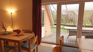 A room with a wooden table and chairs, a floor lamp, and a view of an outdoor deck. - Familienparadies mit Kamin und Terrasse in Babke (Mirow)