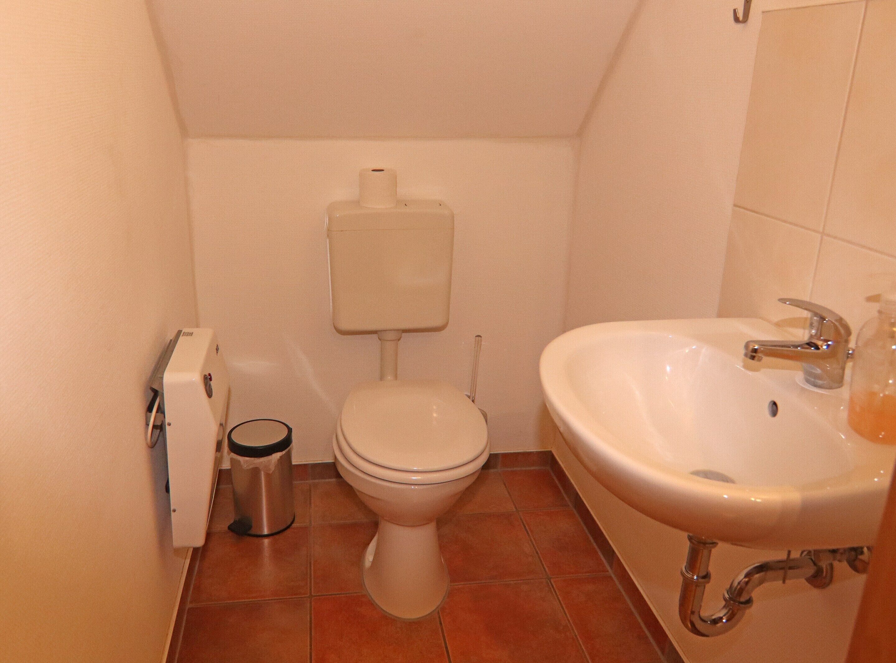 A small bathroom with a toilet, a sink, and a trash can.