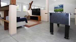 A modern living room with a sofa, TV, and foosball table. - Familienparadies mit Kamin und Terrasse in Babke (Mirow)