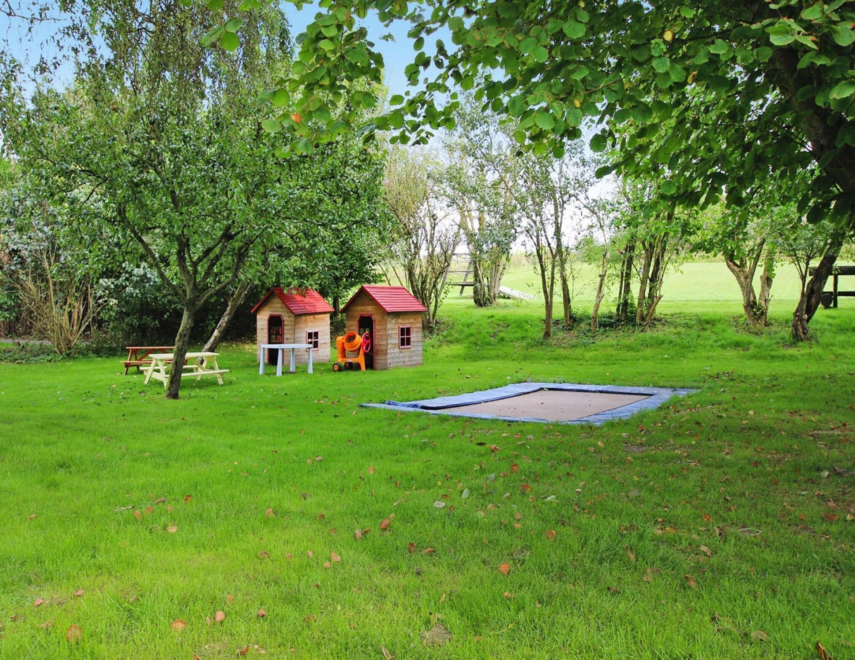 A grassy outdoor area with two small wooden playhouses, a picnic table, and a trampoline.