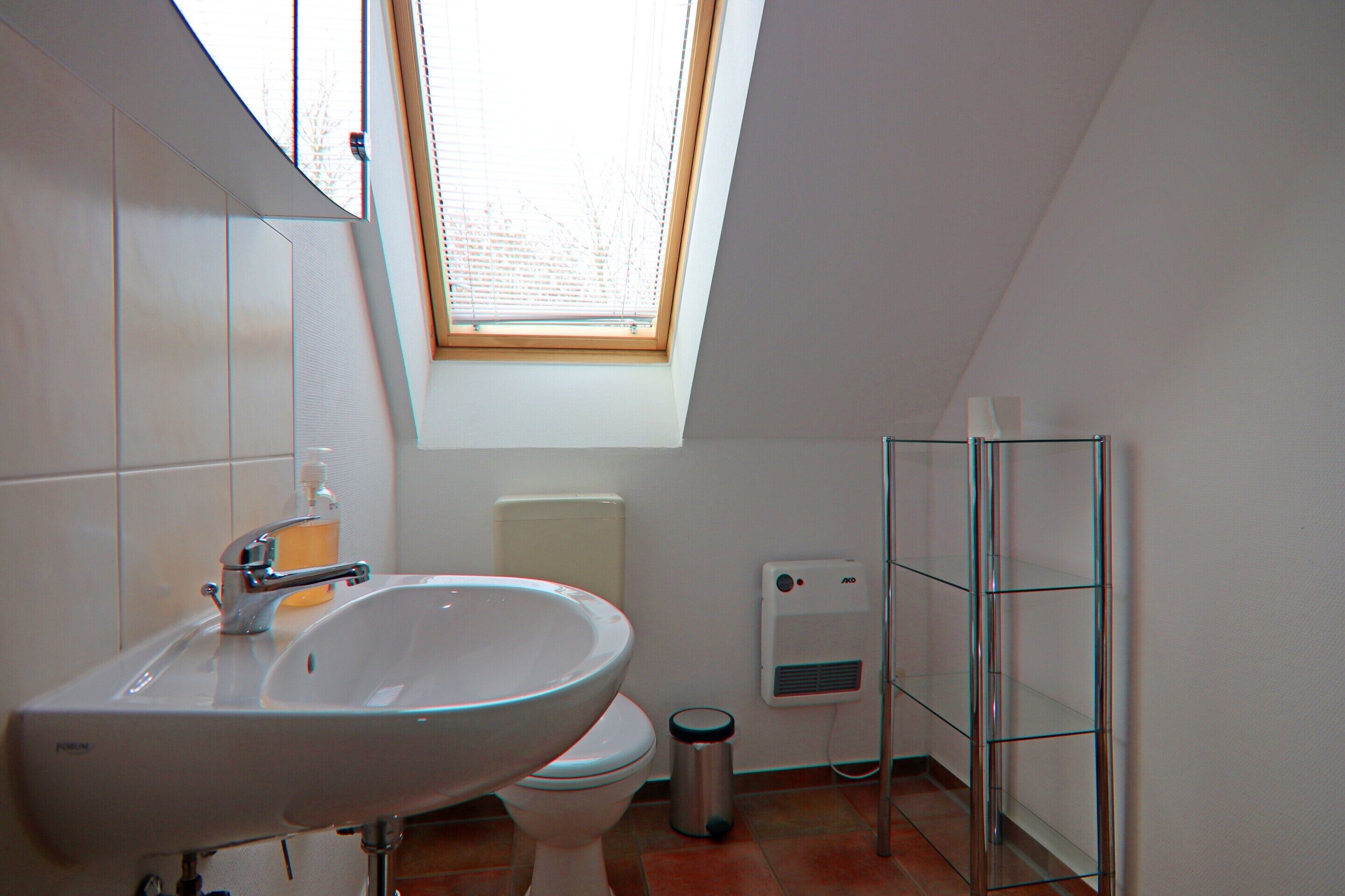 Un baño con tragaluz, un lavabo, un inodoro, un cubo de basura y una cabina de ducha de vidrio.