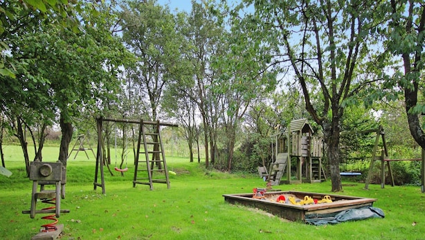 A playground with swings, a slide, and a playhouse in a grassy area with trees. - Familienparadies mit Kamin und Terrasse in Babke (Mirow)