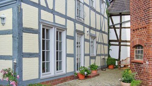 A traditional half-timbered building with a cobblestone courtyard, potted plants, and a bench. - Ferienhaus Rosenhof, Lenzen (Lenzen)