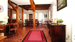 A spacious dining area with wooden furniture, a red rug, and a kitchen area with a wooden cabinet and a plant. - Ferienhaus Rosenhof, Lenzen (Lenzen)