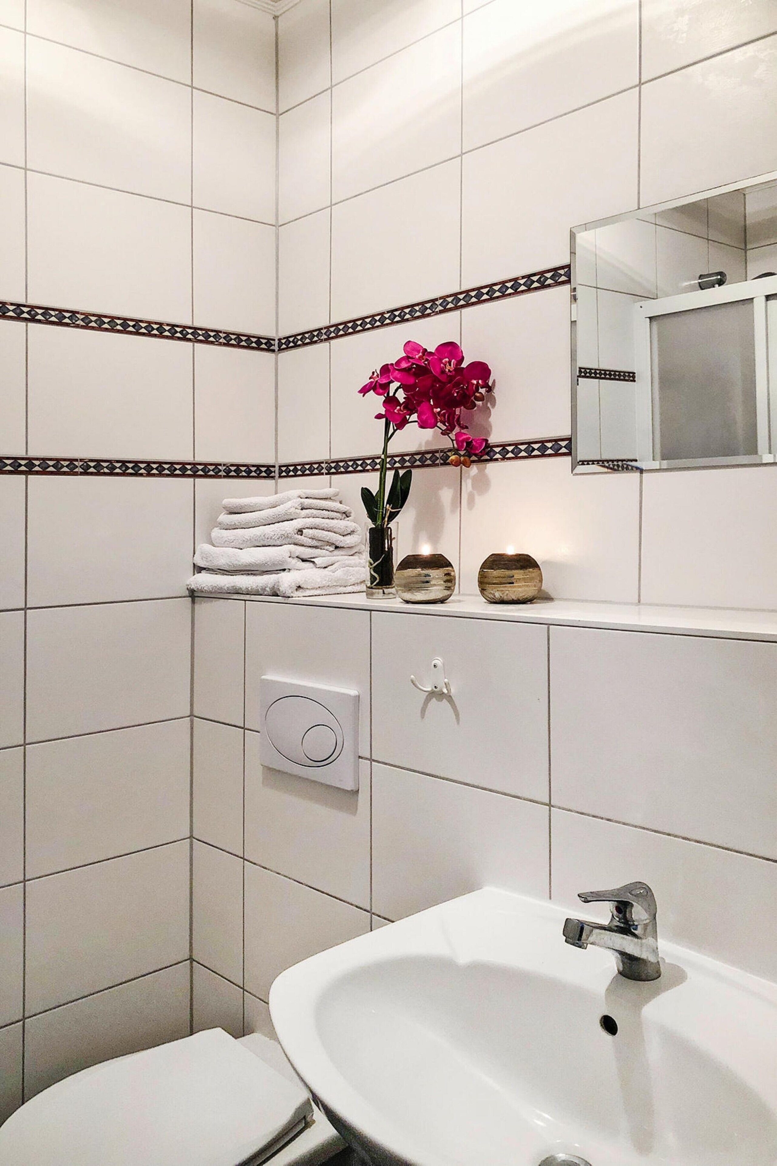 Une salle de bain avec un lavabo blanc, des toilettes, un miroir et un vase décoratif avec des fleurs.