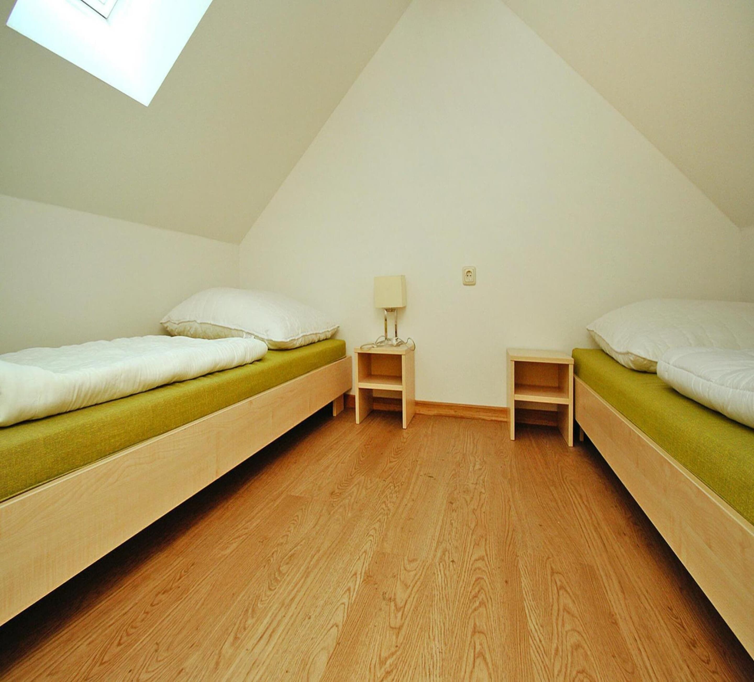 A small, triangular attic bedroom with two bunk beds, a nightstand, and a lamp.