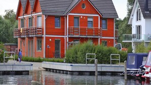 A red two-story house with balconies, a dock, and a small boat. - Ferienwohnung Fewo Elde in Plau am See (Plau am See)