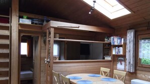 A wooden cabin with a dining area featuring a round table and chairs, a built-in bookshelf, and a skylight. - Ferienhaus in Dornhan (Dornhan)