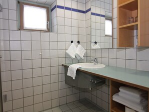 A bathroom with white tiled walls, a sink with a mirror above it, and a towel rack with two towels. - Apartments, Gohren (Göhren)