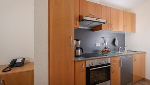 A modern kitchen with wooden cabinets, a built-in oven, a coffee maker, and a sink. - Apartments, Gohren (Göhren)