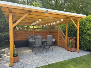 A wooden pergola with a tiled patio, two tables, and chairs. - Ferienwohnung in Moorhusen (Sudbrookmerland)