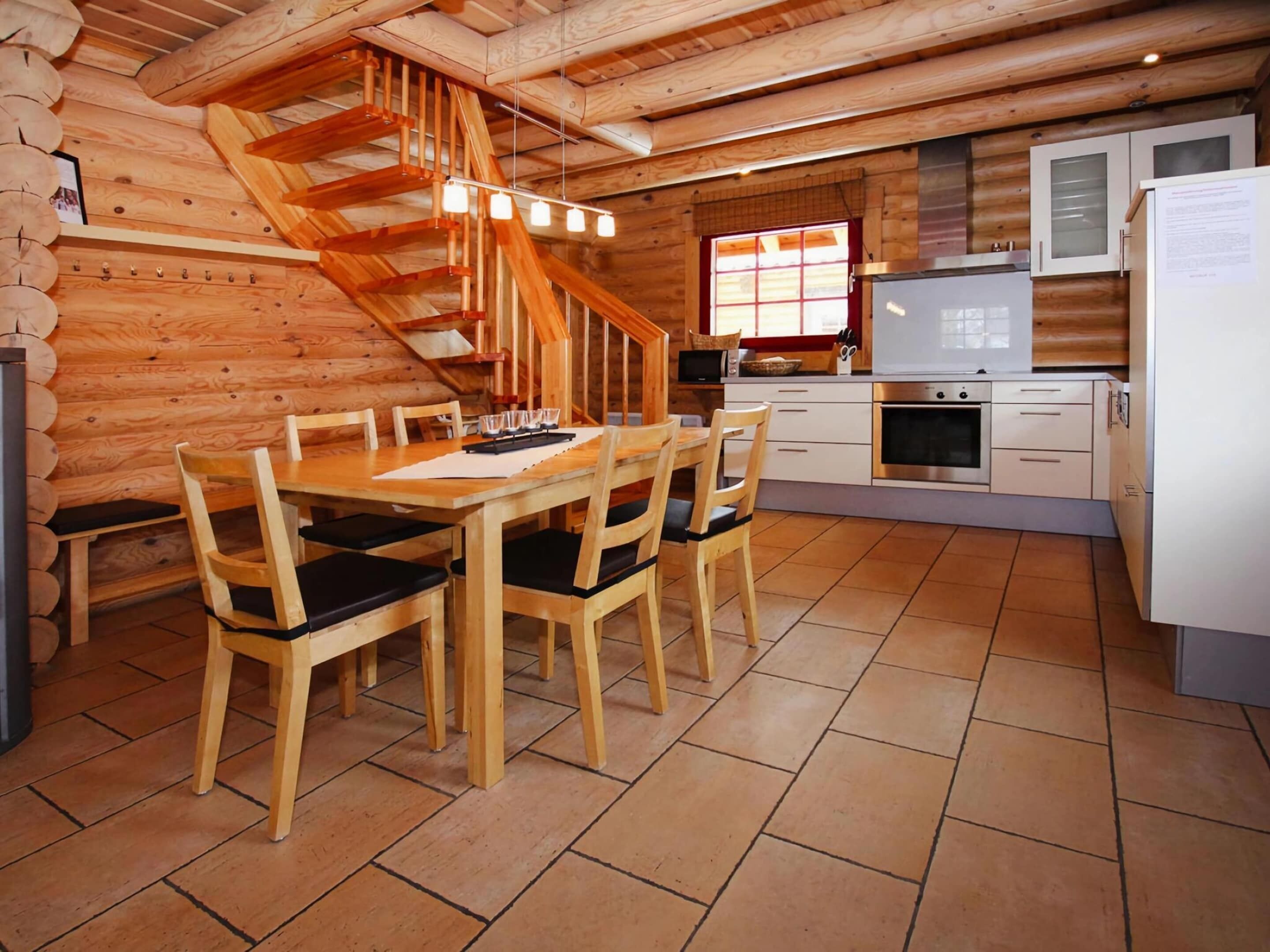 Ein Holzblockhaus-Innenraum mit Essbereich, Küche und einer Holztreppe.