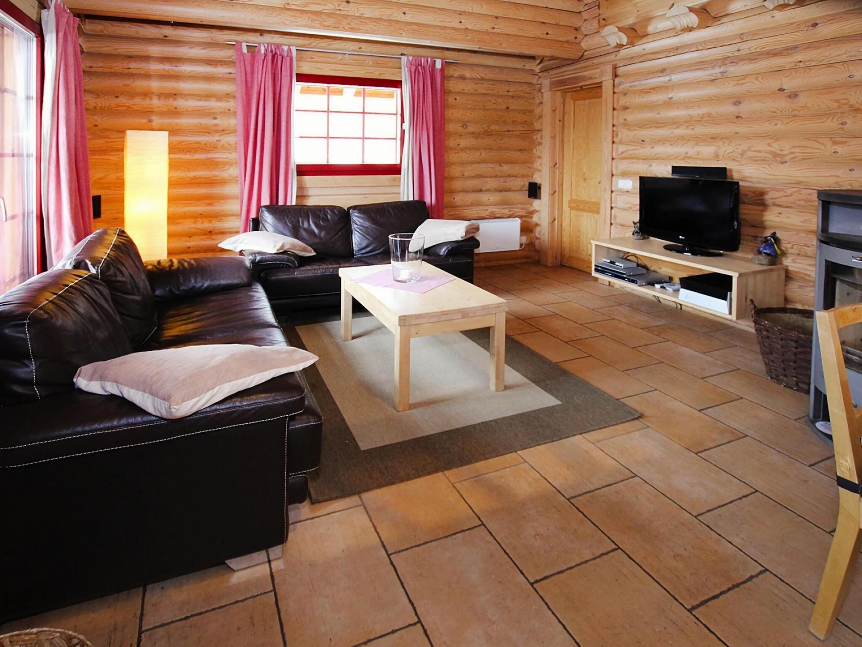 Acogedor interior de una cabaña de madera con un sofá de cuero, una mesa de centro de madera, un televisor sobre un mueble de madera y una chimenea.