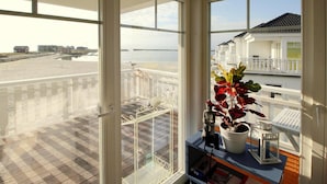 Un balcon avec vue sur la plage et l’océan, une balustrade blanche et un pot de fleurs.