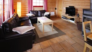 A cozy log cabin interior with a leather sofa, a wooden coffee table, a television, and a fireplace. - Ferienhaus in Schierke mit Garten (Wernigerode)