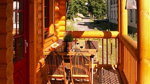 A log cabin with a wooden porch, a red door, and a view of a street and greenery. - Ferienhaus in Schierke mit Garten (Wernigerode)