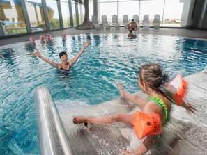 En indendørs swimmingpool med klart vand, en livreddersstol og et bassinområde med udsigt til det fri.