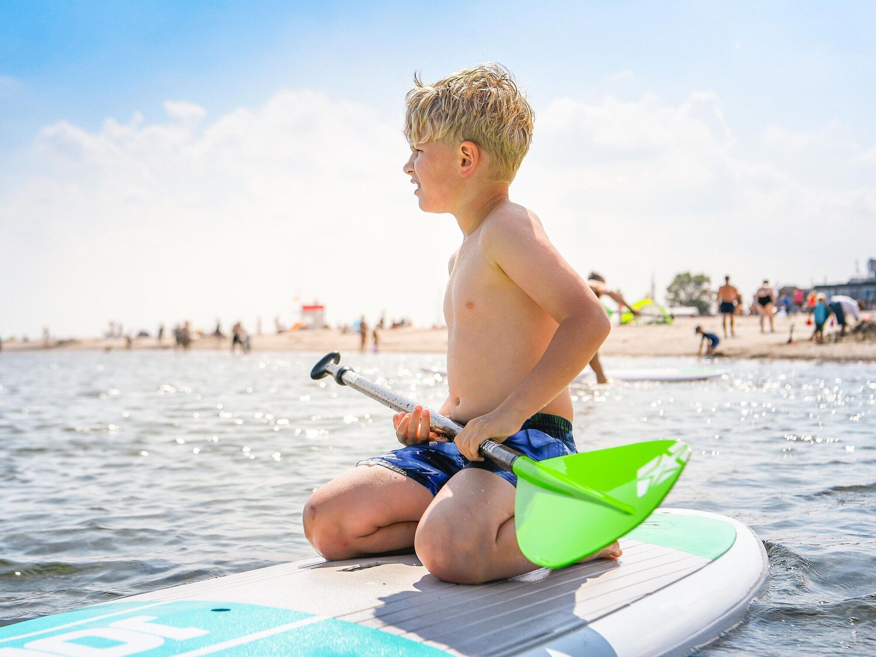 A person sitting on a paddleboard in a body of water with a beach in the background.