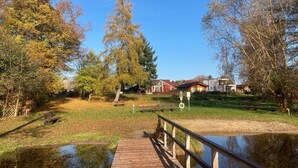 Eine Holzbrücke über einen Teich mit einer Rasenfläche und Bäumen im Hintergrund.