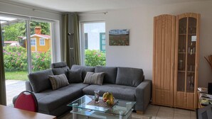 Ein modernes Wohnzimmer mit einem grauen Ecksofa, einem Glastisch und einer Holzkommode.