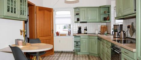 A kitchen with green cabinets, a wooden dining table with chairs, and a hanging light fixture.