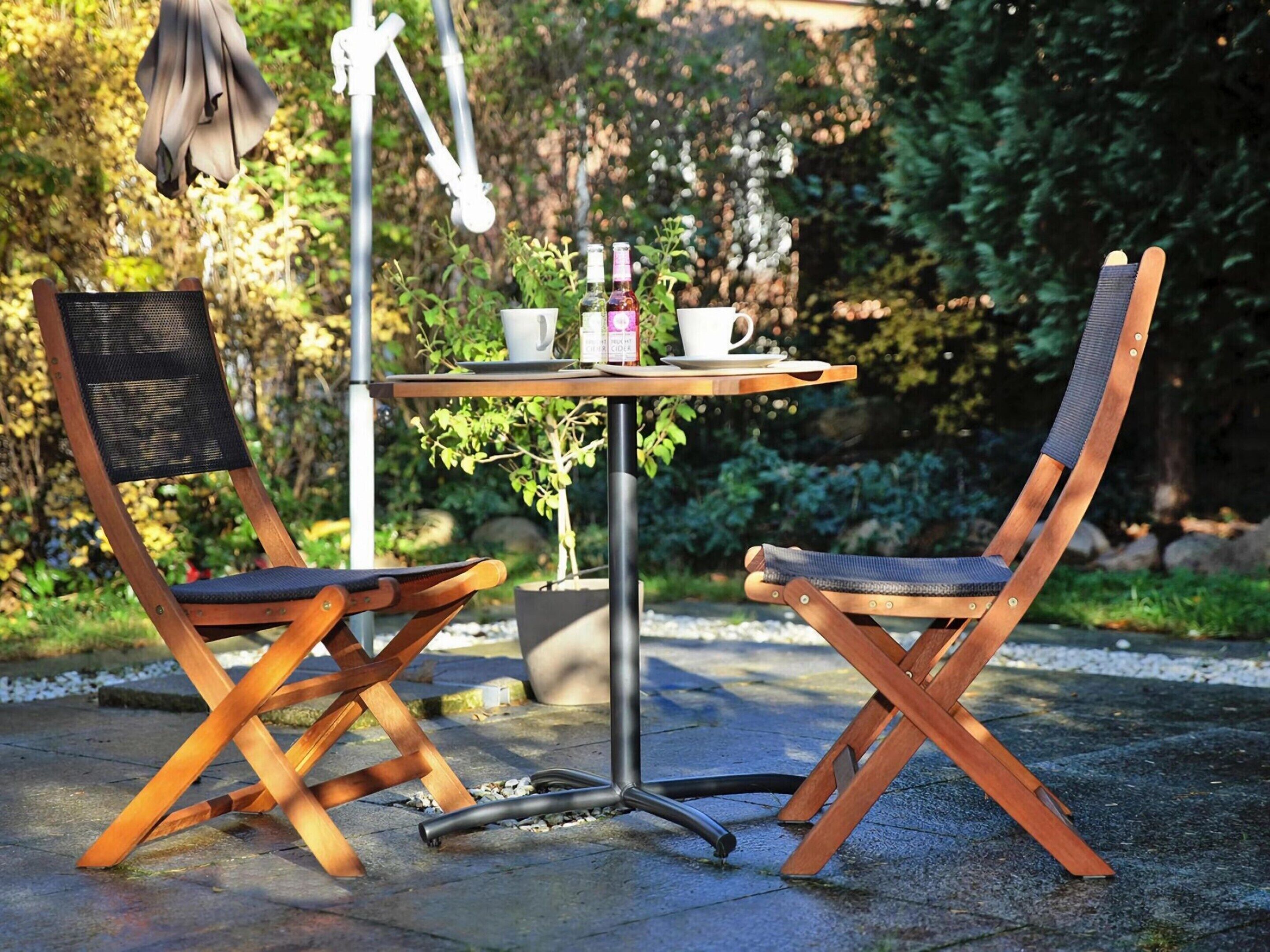 A wooden outdoor table with two chairs, a white mug, and a bottle of water.