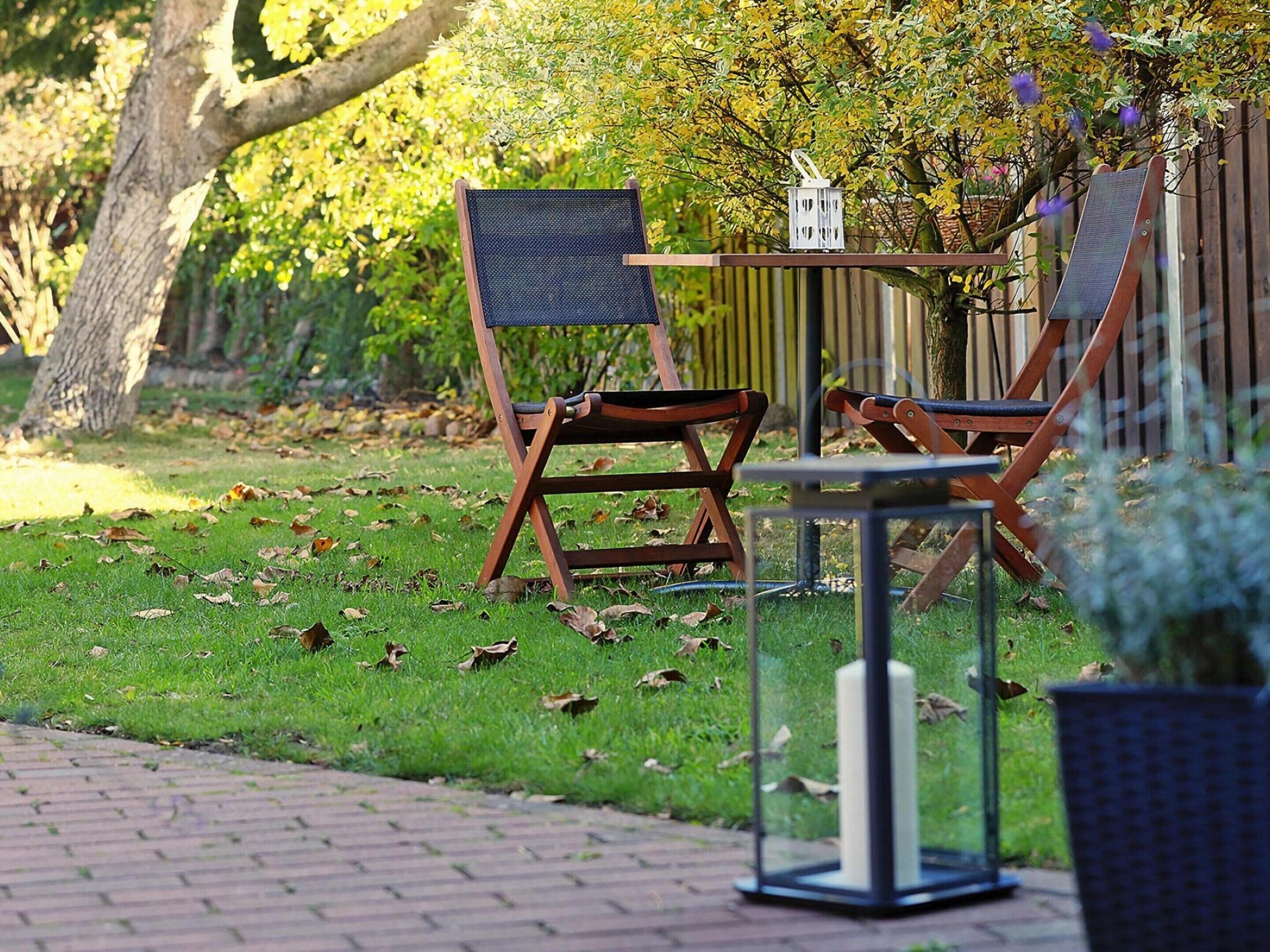 Un espace extérieur aménagé avec une table et deux chaises, entouré d’un jardin agrémenté d’un arbre et d’une clôture.