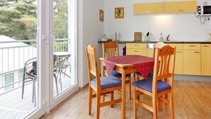 A dining area with a table and chairs, a kitchen with yellow cabinets, and a view through a glass door. - Appartementhaus, Zinnowitz (Zinnowitz)