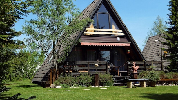 A wooden cabin with a triangular roof, large windows, and a porch with benches. - Ferienpark Tennenbronn (Schramberg)