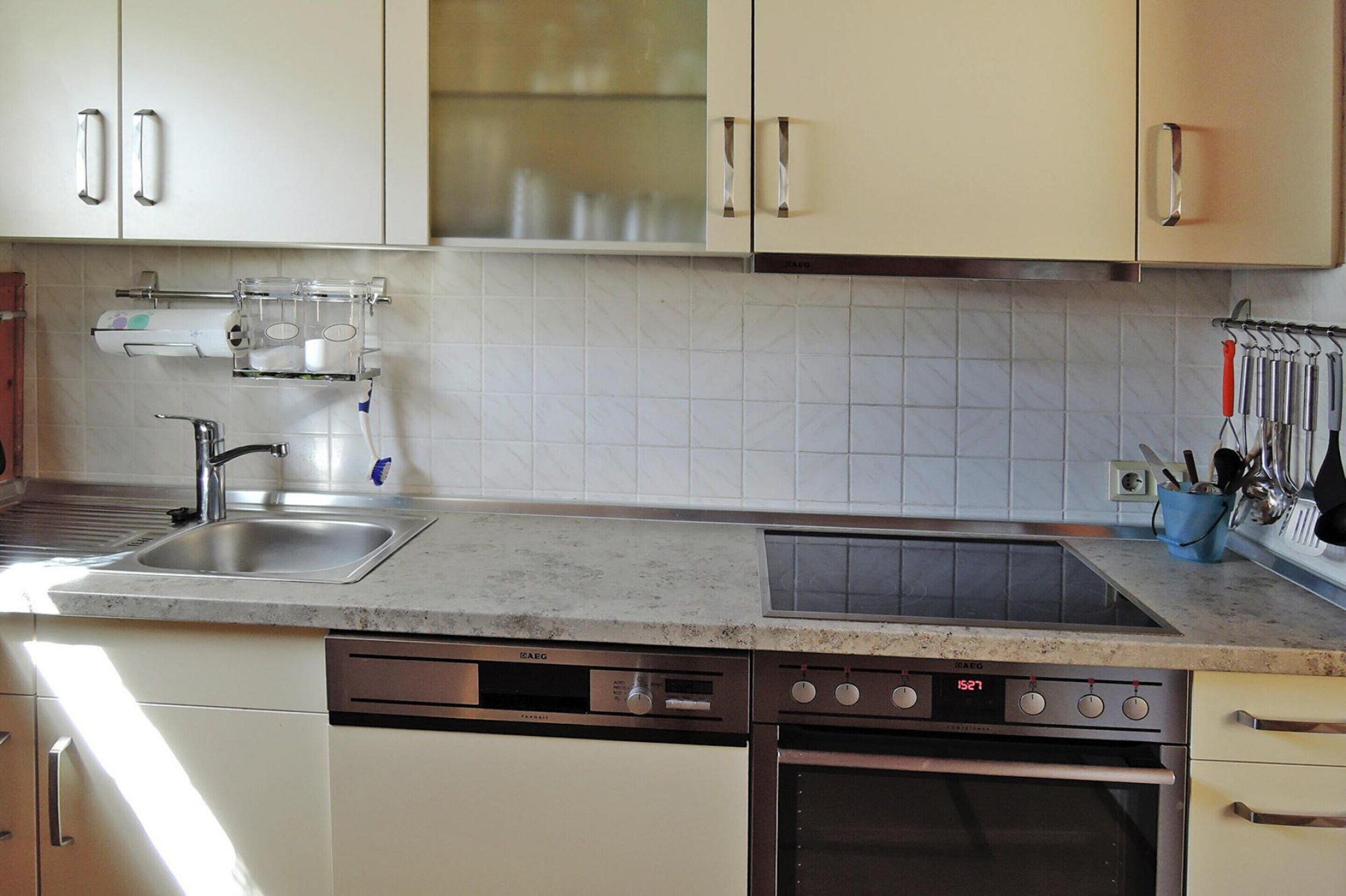 Eine moderne Küche mit weißen Schränken, einem eingebauten Geschirrspüler, einem Backofen und einer Spüle aus Edelstahl.